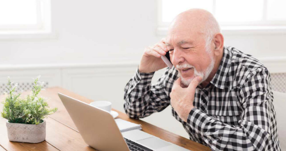 Man sitting at table talking on the phone next to a laptop